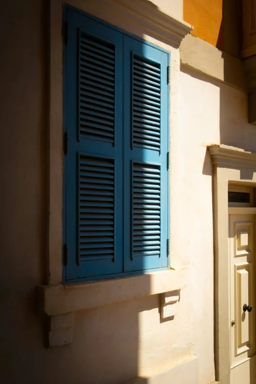 Blue shuttered window on sunlit Mediterranean wall